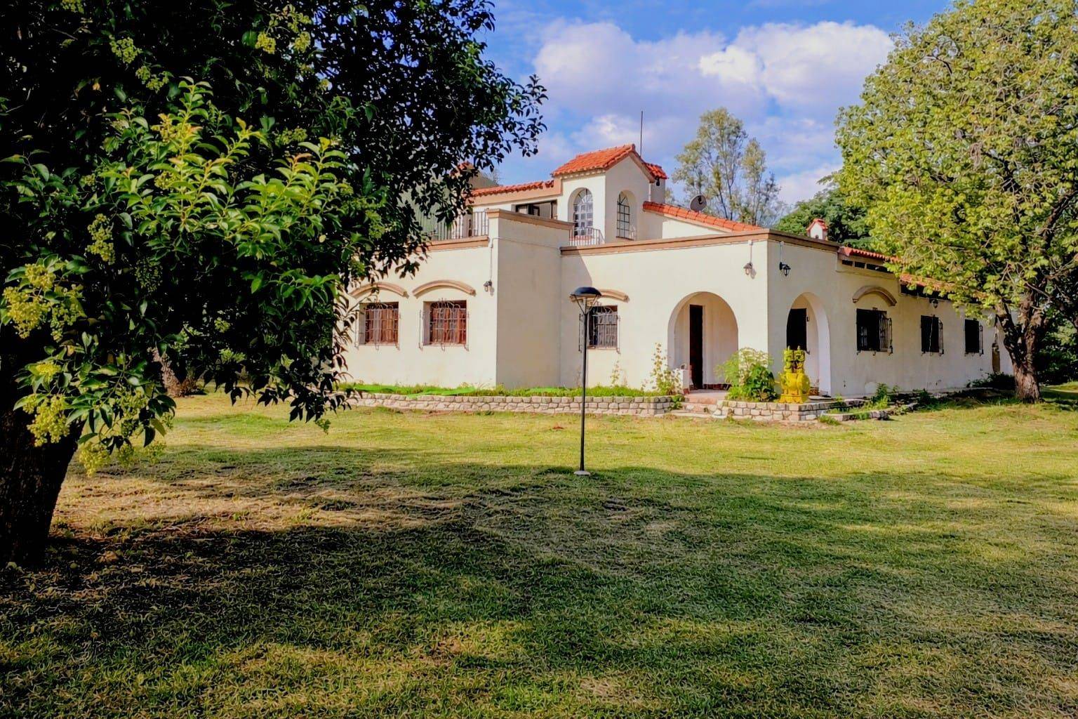 Frente de la casa quinta, de paredes blancas, arcos y tejas, con el parque adelante